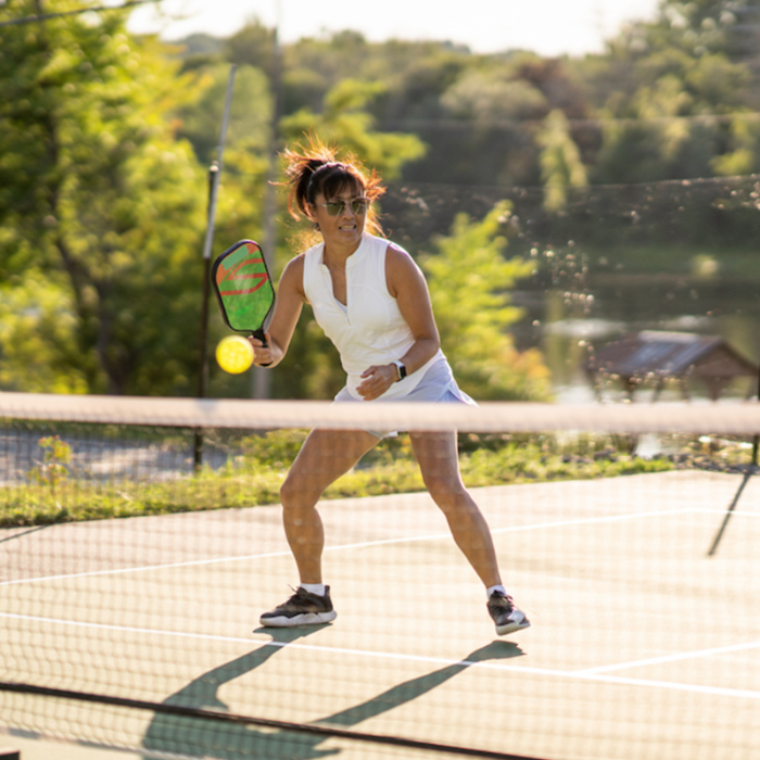 Woman playing pickleball on an outdoor court with trees in the background